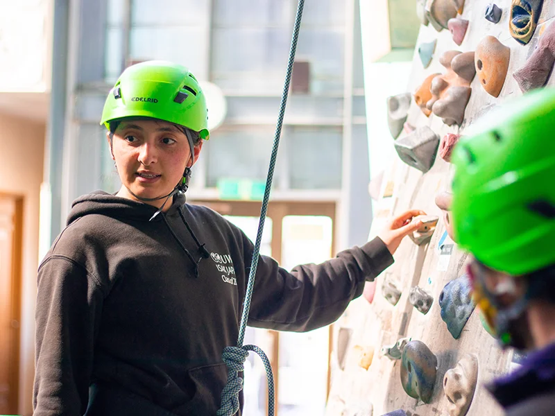 Students wearing helmets climb across rocks during an outdoor education activity